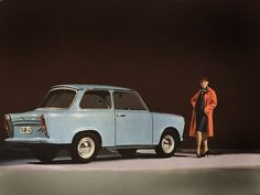 a woman standing next to a blue car in front of a black background with an orange coat on