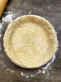 an uncooked pie crust sitting on top of a wooden table next to a rolling pin