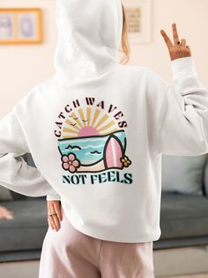 Catch Waves, Not Feels in this cute surfer Hoodie! Crafted from a comfy cotton and polyester blend, this sweatshirt ensures all-day comfort whether you're lounging by the bonfire or just hanging out on the couch. The design features a charming combination of pastel hues and adorable surf-inspired graphics, including flowers, a beachy sunset, and of course, a surfboard. Whether you're a seasoned surfer or just dreaming of seaside adventures, this shirt is sure to become your go-to choice for effortless beach chic. Care Instructions: Machine wash: warm (max 40C or 105F); Bleach as needed; Tumble dry: medium; Iron, steam or dry: low heat; Do not dryclean. Colors may vary slightly compared to what you may see on your computer or phone.  Sizing is unisex and runs true to size; see size chart in White Cotton Beach Hoodie, White Cotton Hoodie For Beach, White Cotton Hoodie For The Beach, Casual Beach Hoodie Top, Casual White Hoodie For Beach Season, Beach Season Graphic Print Hoodie Sweatshirt, White Letter Print Hoodie For Beach, Trendy Graphic Print Hoodie For Beach Season, Casual Surfing Hoodie With Graphic Print