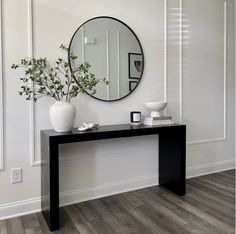 a black and white console table with a round mirror on the wall next to it