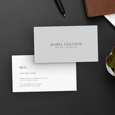 two white business cards sitting on top of a desk next to a pen and plant