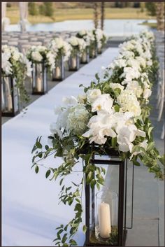 an outdoor ceremony with white flowers and greenery on the aisle, lit by candles