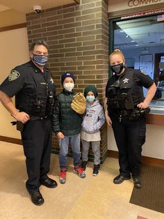 three police officers standing in front of a window with children wearing face masks and gloves