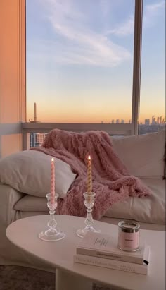 two candles sitting on top of a white table next to a couch with a pink blanket