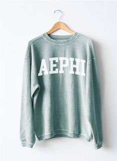 a green sweatshirt with the word aephi on it hanging from a wooden hanger