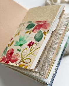 an open book with flowers on it sitting on a table next to scissors and thread