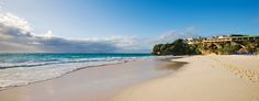 a sandy beach next to the ocean under a blue sky with clouds and buildings in the distance