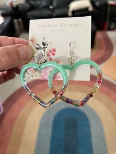 two heart shaped earrings are being held in front of a card with the name rainbow bloomers on it