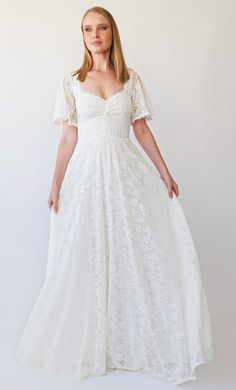 a woman wearing a white dress with short sleeves and a v neckline, standing in front of a white background