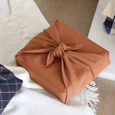 an orange wrapped gift box sitting on top of a white blanket next to other items