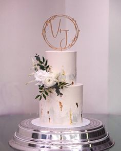 a three tiered white cake with flowers on top and the letter d on it