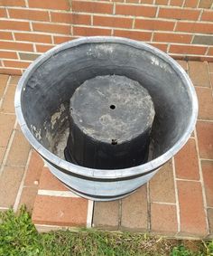 an empty metal bucket sitting on top of a brick floor next to a grass field