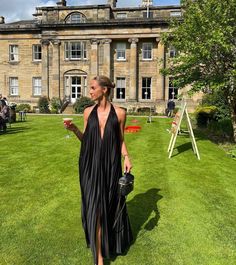 a woman in a black dress is walking through the grass