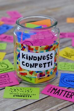 a glass jar filled with lots of colorful sticky notes on top of a wooden table