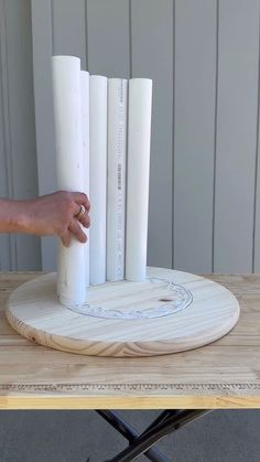 a person is holding up a piece of paper on top of a wooden table with four white columns