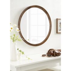 a round mirror sitting on top of a white table next to a vase with flowers