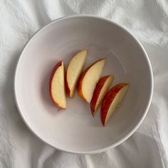 four pieces of apple in a white bowl on a white cloth covered tablecloth, top view