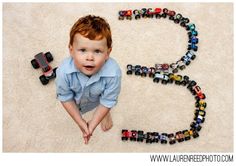 a young boy sitting on the floor next to a train track made out of toy cars