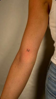 a woman's arm with the letter m tattooed on her left arm, in front of a white background