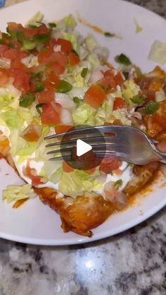 a white plate topped with food and a fork on top of a marble countertop