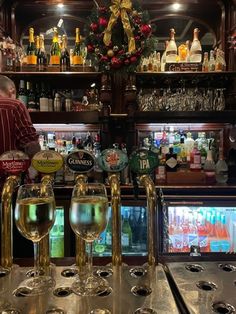 several glasses of wine sit on the bar at a christmas - themed pub, with liquor bottles in the background