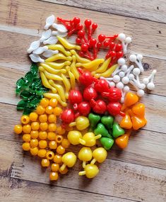 many different colored plastic fruits and vegetables on a wooden surface with white, red, yellow, green, orange, and black beads