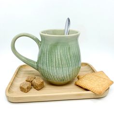 a green coffee cup and some crackers on a wooden tray with a white background