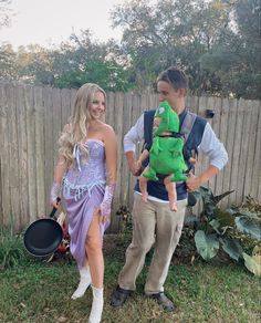 a man and woman in costumes holding a baby while standing next to a garden fence