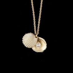 a necklace with a shell on it and a pearl hanging from the front, against a black background