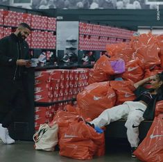 two men standing next to piles of orange bags