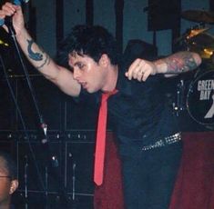 a man in a black shirt and red tie with his arms stretched out as he sings into a microphone