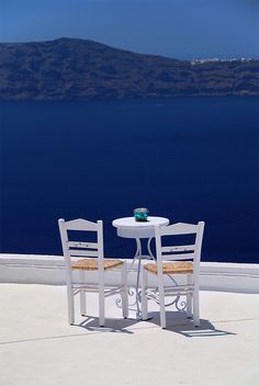 two chairs and a table on a balcony overlooking the ocean