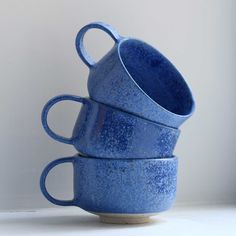 three blue mugs stacked on top of each other in front of a white wall