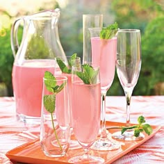 three glasses filled with pink liquid and mint sprigs sit on a wooden tray