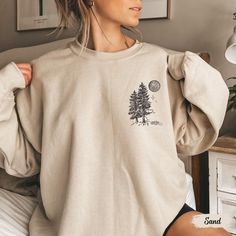 This sweatshirt, featuring a pocket design with pine trees and a moon, is a must-have for wilderness lovers and granola girls alike. Whether you're hiking, camping, or simply embracing your love for nature, this crewneck is the perfect blend of cozy and adventurous! Prefer this design on a T-Shirt? Visit this link: https://bohemianbloomdesigns.etsy.com/listing/1785034623/wilderness-shirt-pine-tree-shirt Prefer this design on a Hoodie? Visit this link: https://bohemianbloomdesigns.etsy.com/listin Oversized Long Sleeve Tops For Outdoor, Long Sleeve Graphic Print T-shirt For Camping, Relaxed Fit Tops With Pockets For Outdoor, Outdoor Cotton Sweatshirt With Pockets, Cotton Sweatshirt With Pockets For Outdoor Activities, Cozy Outdoor Tops With Pockets, Casual Crew Neck Sweatshirt For Adventure, Long Sleeve T-shirt For Fall Adventure, Cozy Crew Neck Tops With Pockets