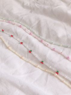 three necklaces are laying on top of a white sheet and one has red beads