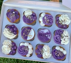 a box filled with cupcakes covered in purple frosting and white icing