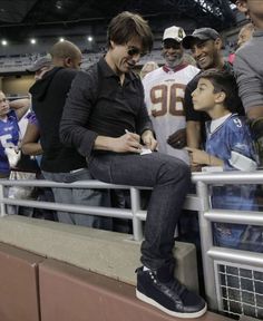 a man sitting on the bleachers at a football game signing autographs for fans