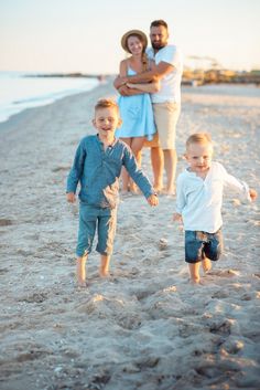 a family walking on the beach holding hands and smiling at the camera with their little boys