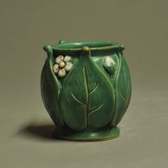 a green vase with white flowers and leaves on the outside, sitting on a gray surface