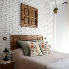 a bedroom with white brick walls and wooden headboard, two pillows on the bed