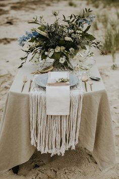 a table set up on the beach with flowers and place settings