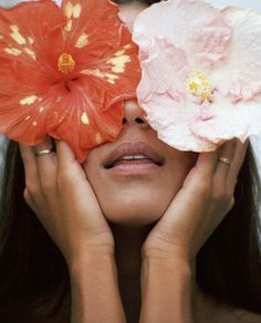 a woman holding two flowers in front of her face and covering her eyes with both hands