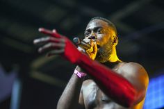 a shirtless man holding a microphone in his right hand and wearing red gloves on the other side