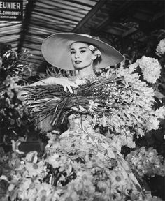 a black and white photo of a woman in a hat surrounded by flowers