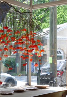 red paper flowers hang from the ceiling in front of a window with cars parked outside