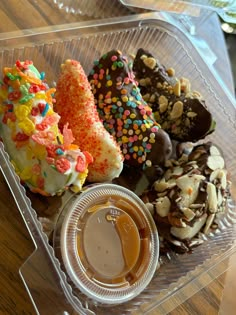 a plastic container filled with lots of different types of donuts on top of a wooden table