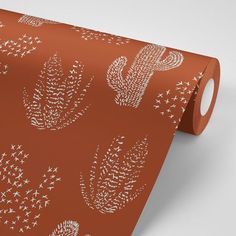 an orange wallpaper with white cactus and stars design on it's side, next to a roll of brown wrapping paper