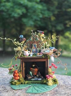 a miniature clock is sitting on top of a stone surface with plants and other things surrounding it