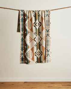 a blanket hanging on a clothes line in front of a white wall and wooden floor